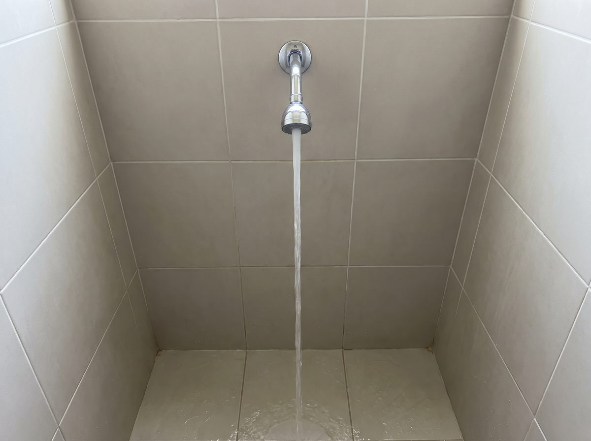 A plain single-spray shower head running in a tiled shower